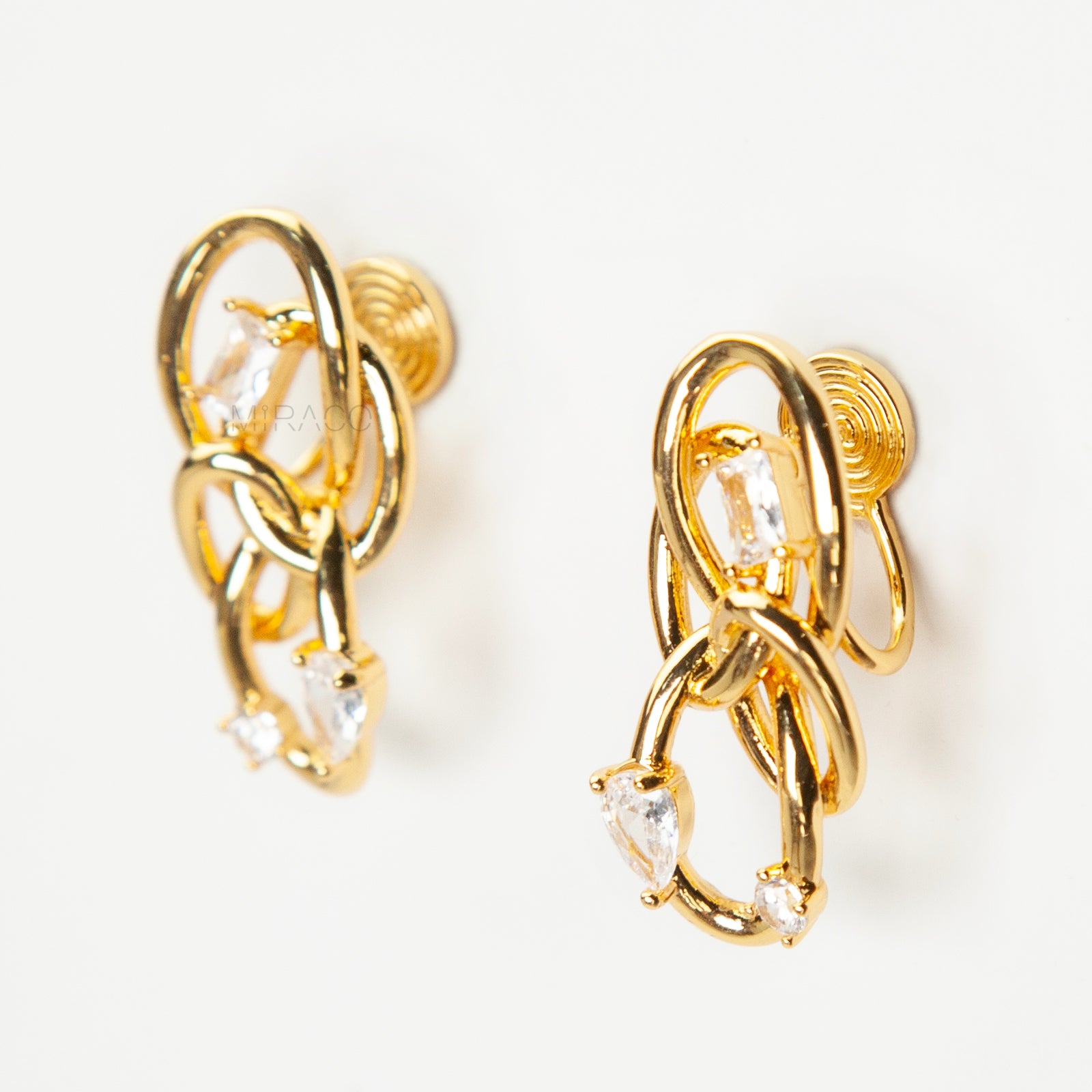 Close-up of a pair of gold interlocking double-knot clip-on earrings featuring two brilliant cut cubic zirconia stones, displayed on a white surface.