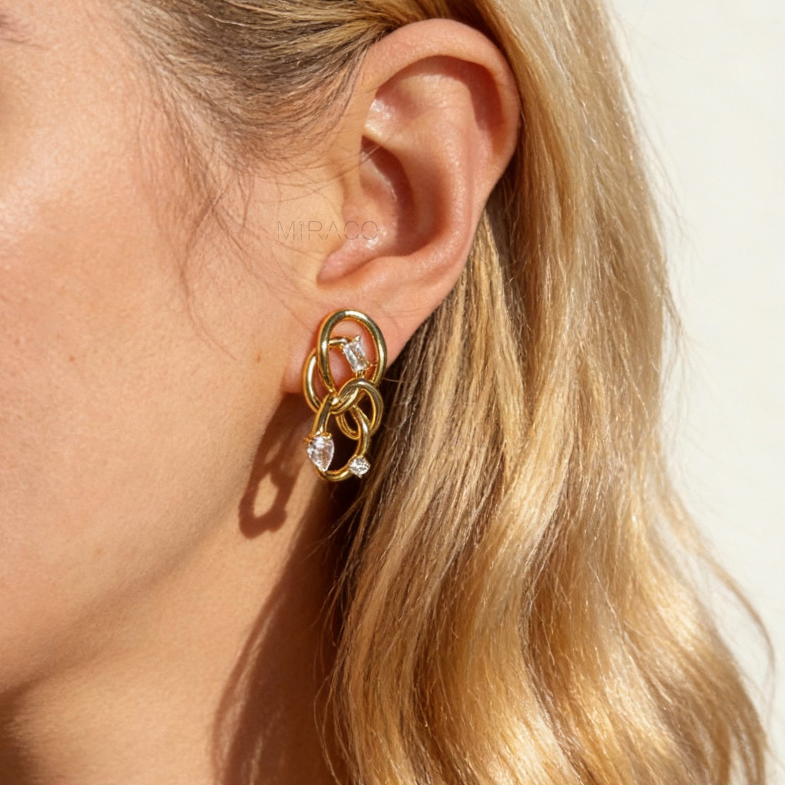 Model wearing a single gold interlocking double-knot clip-on earring with CZ stones, showing the size and fit on a non-pierced ear.