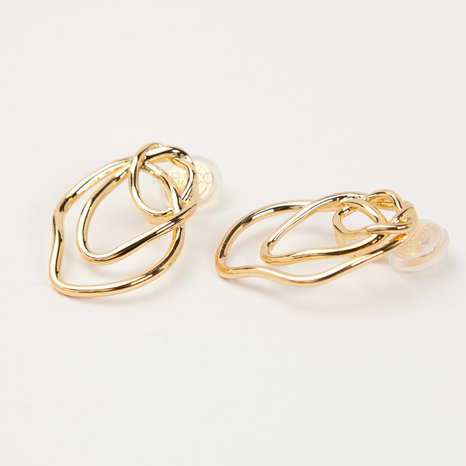 Close-up of comfortable gold-tone interlocking clip-on earrings featuring a modern, abstract double-ring design and a secure clear coil back closure. Non-pierced statement jewelry.