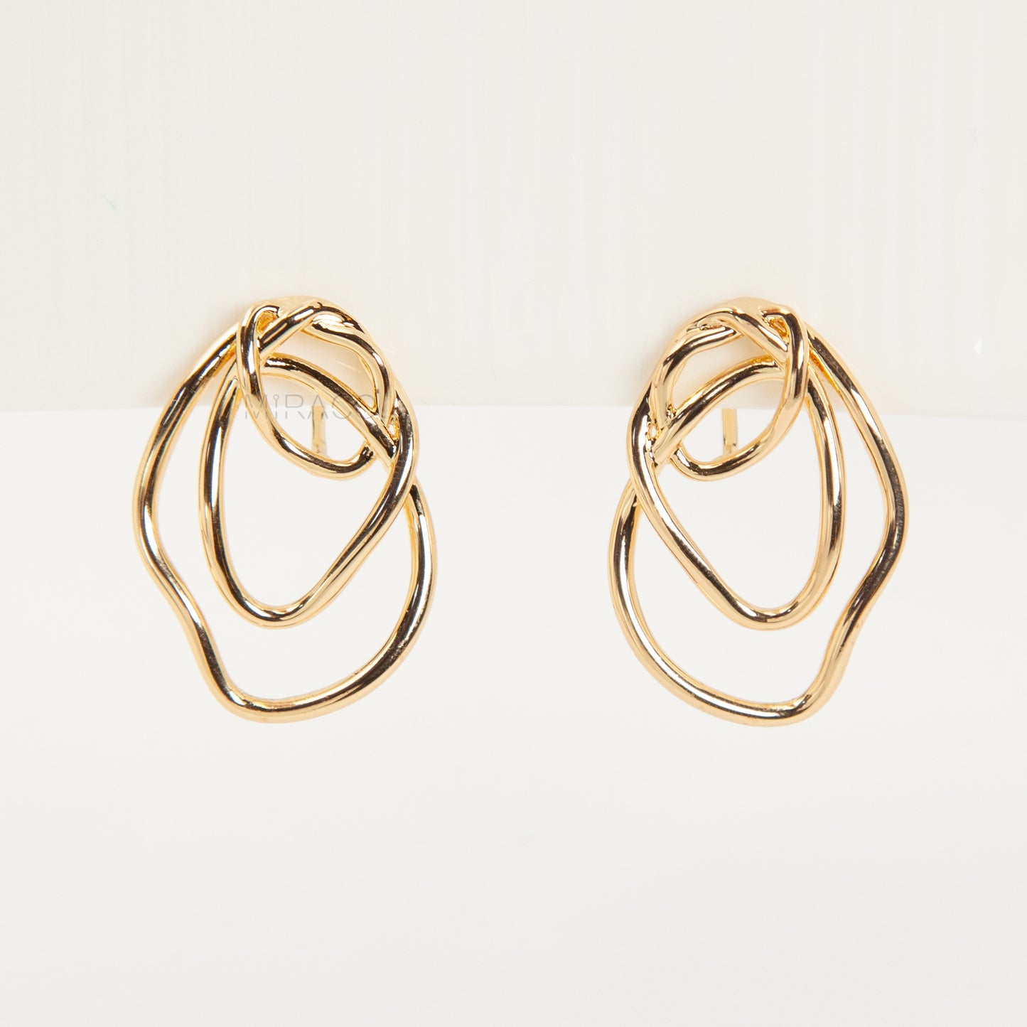Close-up of comfortable gold-tone interlocking clip-on earrings featuring a modern, abstract double-ring design and a secure clear coil back closure. Non-pierced statement jewelry.
