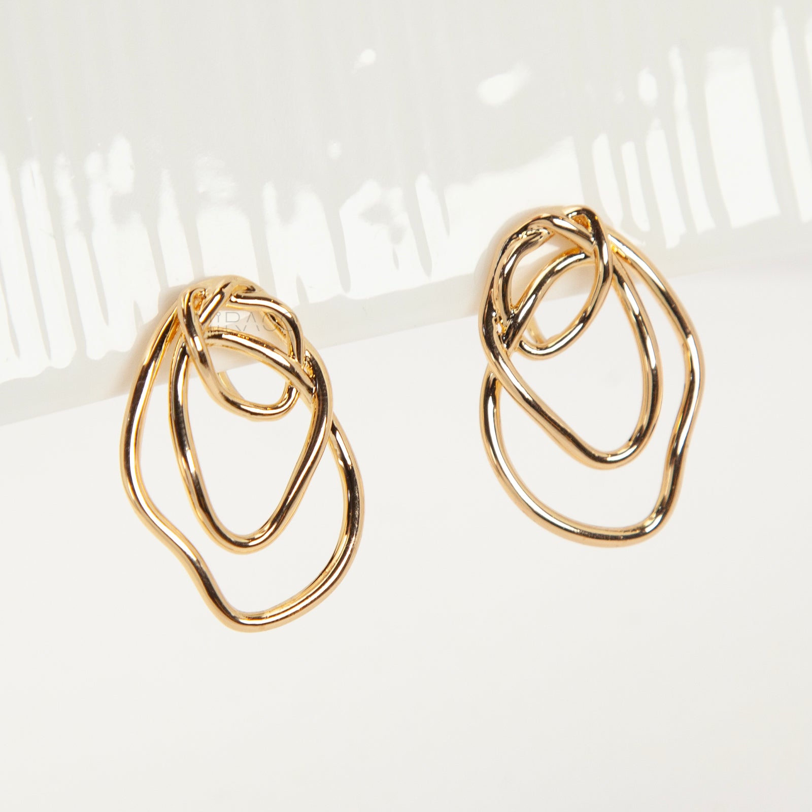 Close-up of comfortable gold-tone interlocking clip-on earrings featuring a modern, abstract double-ring design and a secure clear coil back closure. Non-pierced statement jewelry.