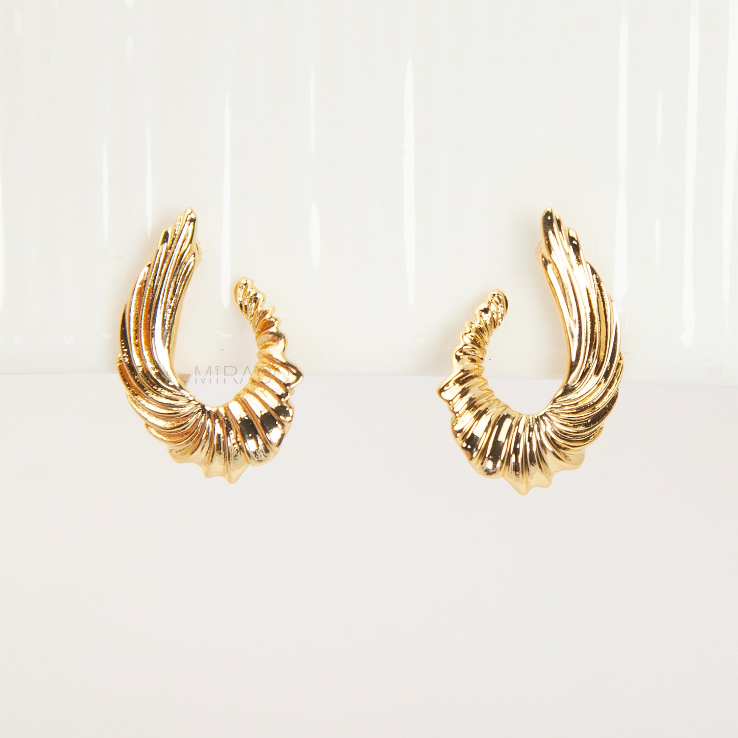 Close-up of comfortable gold-tone clip-on earrings with a ribbed, sculpted croissant or teardrop shape, worn on a model's ear. Features a secure coil back.