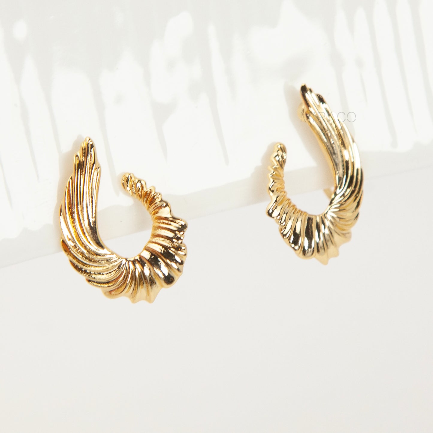 Close-up of comfortable gold-tone clip-on earrings with a ribbed, sculpted croissant or teardrop shape, worn on a model's ear. Features a secure coil back.