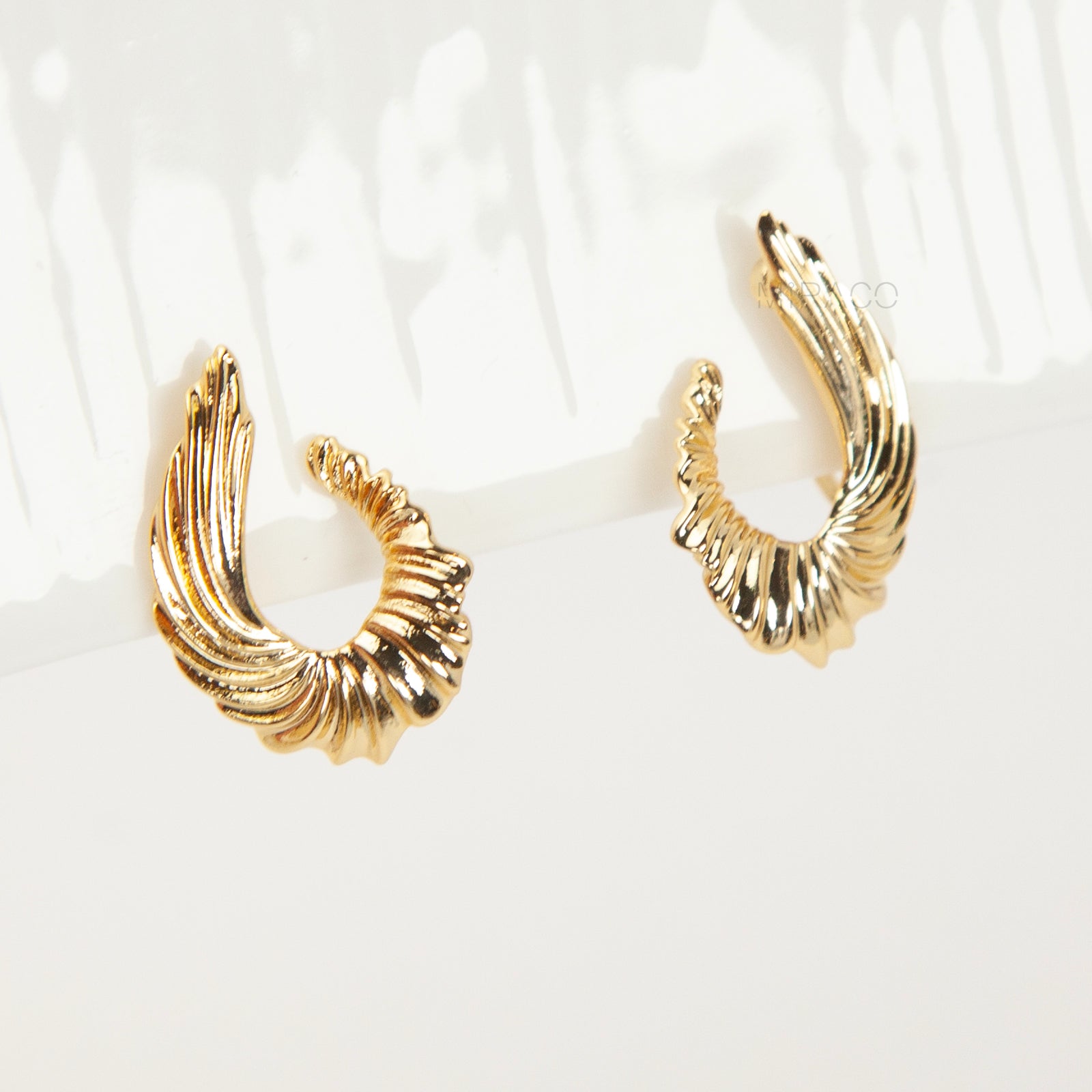 Close-up of comfortable gold-tone clip-on earrings with a ribbed, sculpted croissant or teardrop shape, worn on a model's ear. Features a secure coil back.