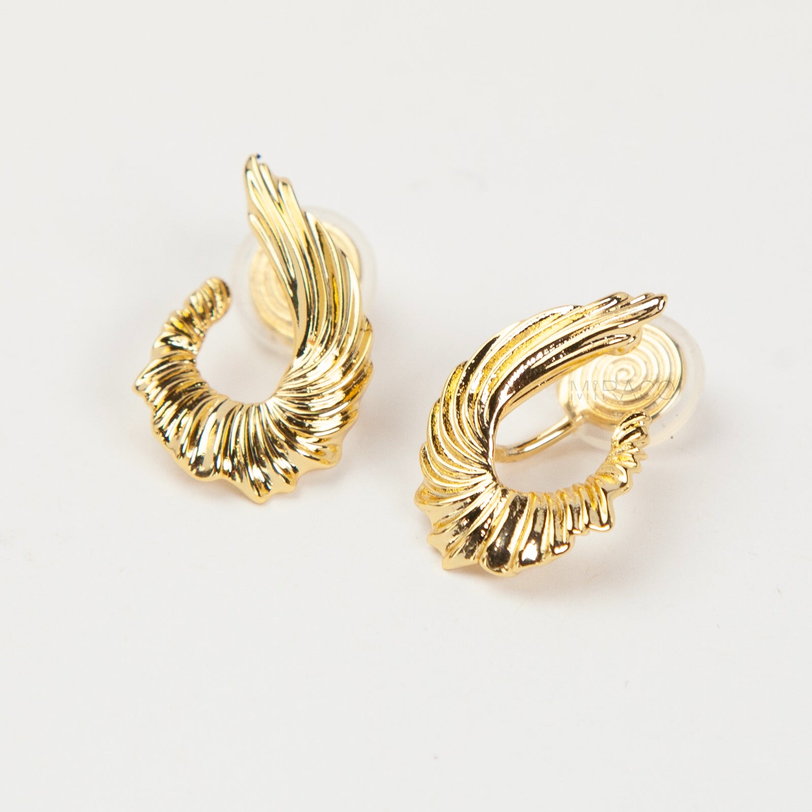 Close-up of comfortable gold-tone clip-on earrings with a ribbed, sculpted croissant or teardrop shape, worn on a model's ear. Features a secure coil back.