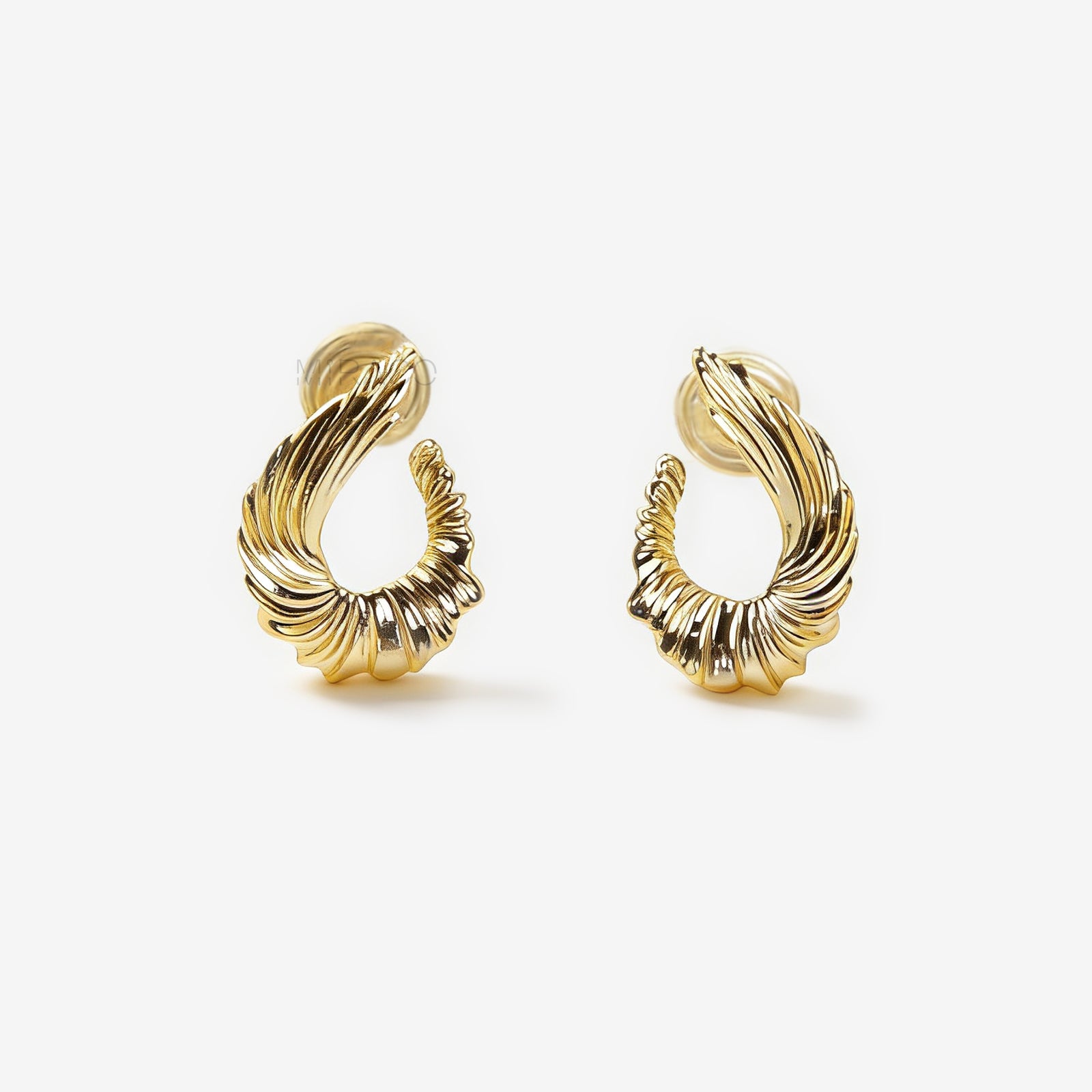 Close-up of comfortable gold-tone clip-on earrings with a ribbed, sculpted croissant or teardrop shape, worn on a model's ear. Features a secure coil back.