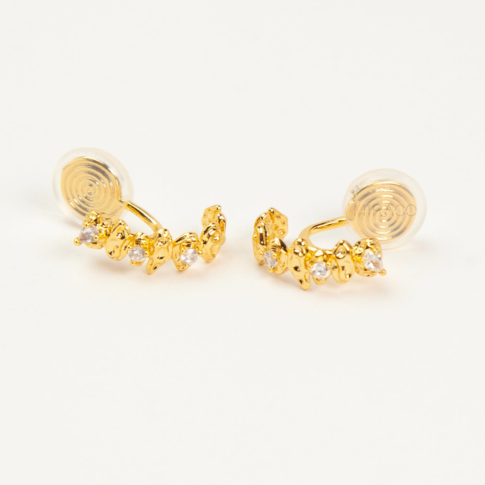 Close-up of gold crescent clip-on earrings with clear cubic zirconia stones and spiral coil backs on a white background.