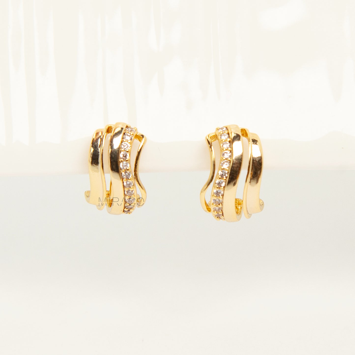 Close-up of gold-tone clip-on earrings featuring a modern stacked band design with a row of small clear crystals and a spiral coil-back.