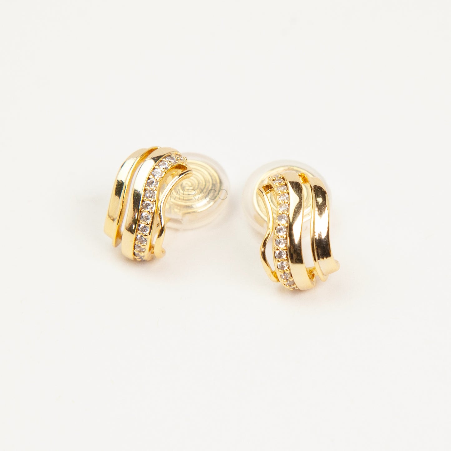 Close-up of gold-tone clip-on earrings featuring a modern stacked band design with a row of small clear crystals and a spiral coil-back.