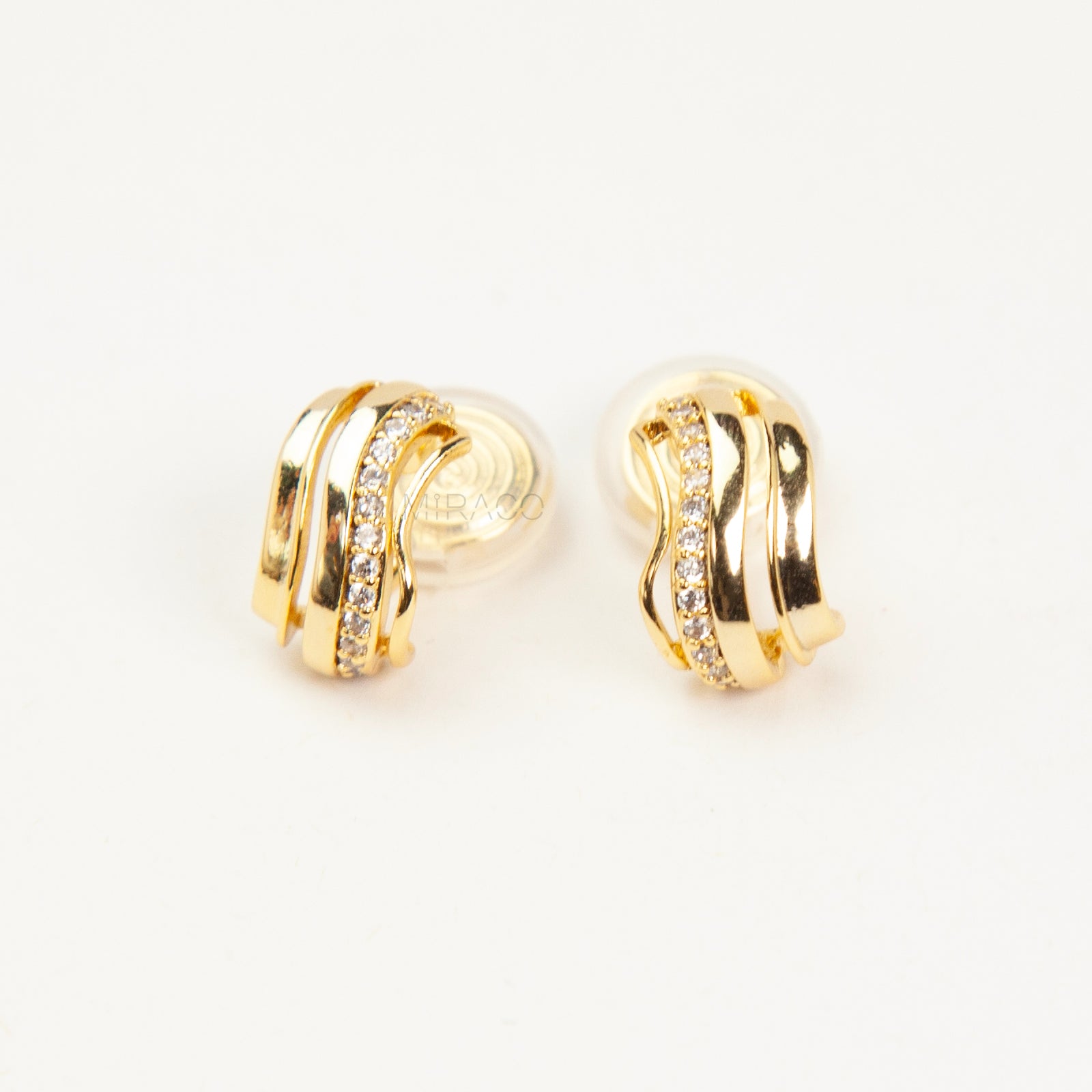 Close-up of gold-tone clip-on earrings featuring a modern stacked band design with a row of small clear crystals and a spiral coil-back.