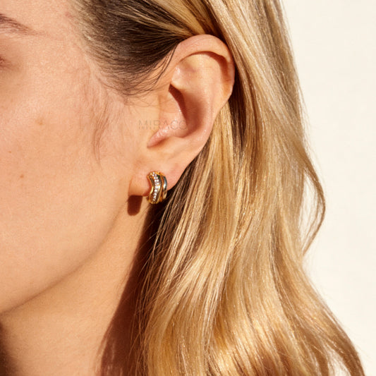 Close-up of gold-tone clip-on earrings featuring a modern stacked band design with a row of small clear crystals and a spiral coil-back.