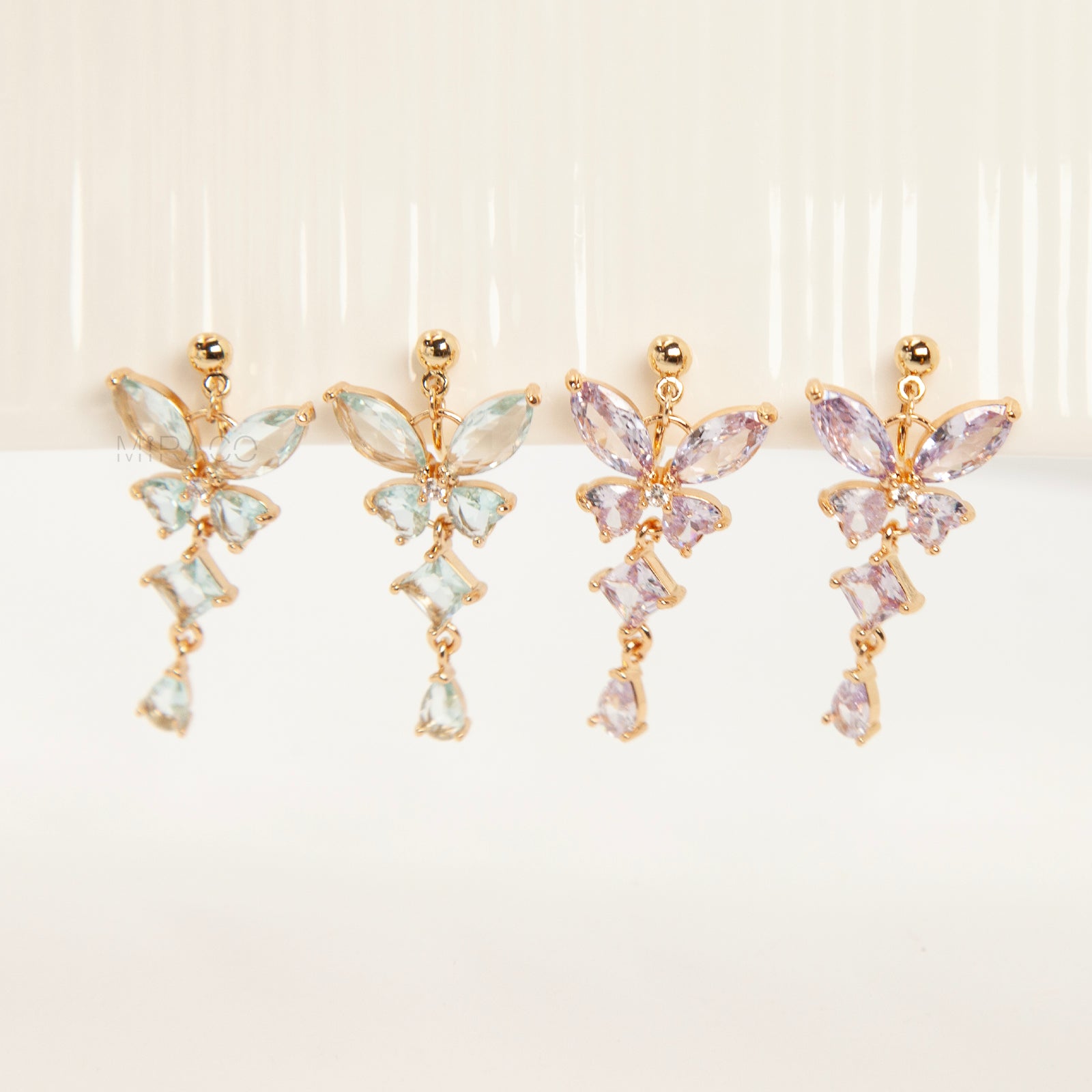 A pair of gold-tone, coil-back clip-on dangle earrings featuring a butterfly cluster of multifaceted Serene Aquamarine (pale blue) crystals and cascading drop stones.