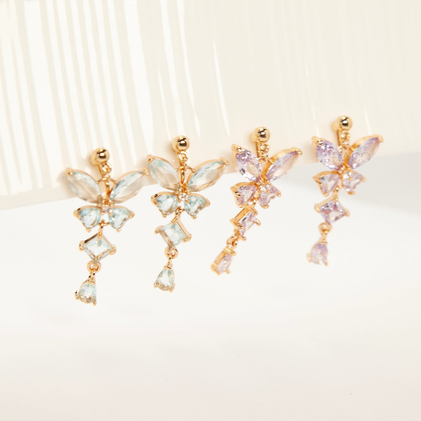 A pair of gold-tone, coil-back clip-on dangle earrings featuring a butterfly cluster of multifaceted Serene Aquamarine (pale blue) crystals and cascading drop stones.