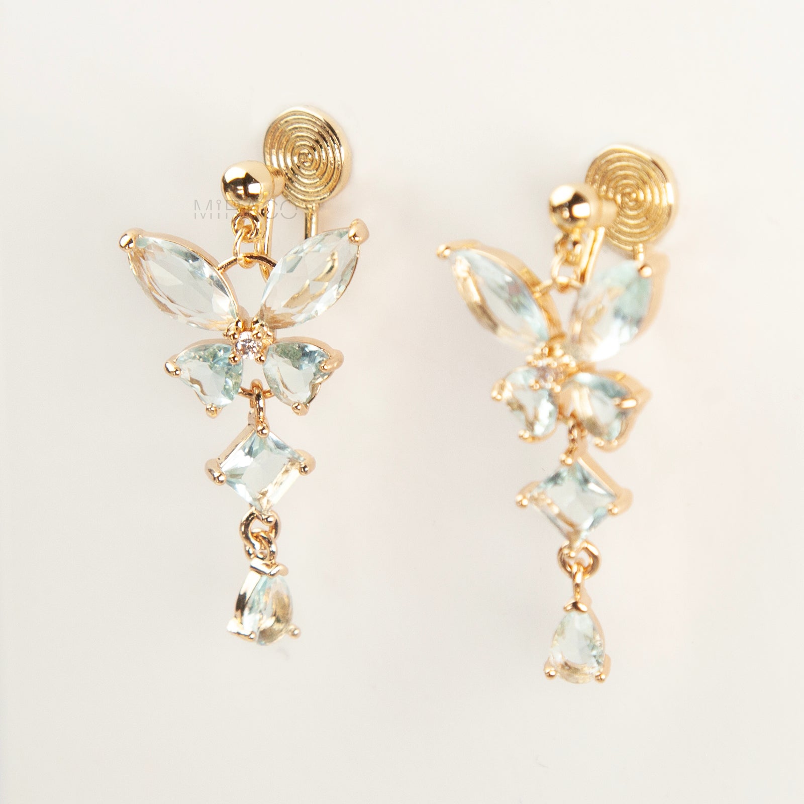 A pair of gold-tone, coil-back clip-on dangle earrings featuring a butterfly cluster of multifaceted Serene Aquamarine (pale blue) crystals and cascading drop stones.
