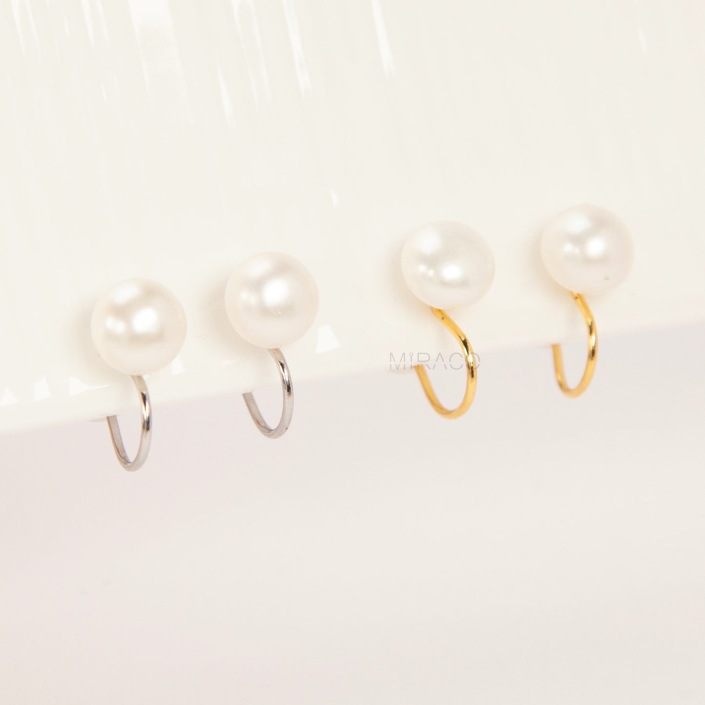 round freshwater pearl clip-on earrings with clear silicone comfort backs, shown in both gold-plated and silver-plated finishes on a white background.