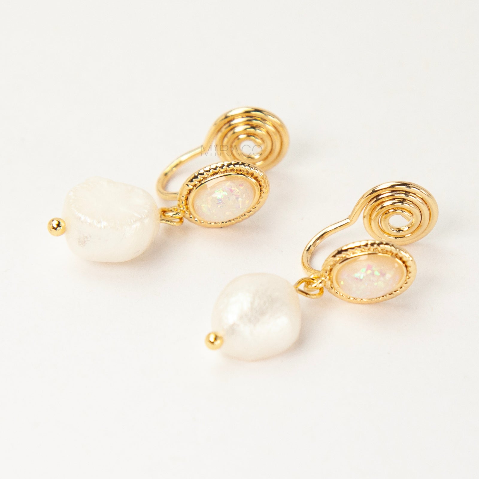 Pair of gold-tone, coil-back clip-on earrings with an oval, bezel-set iridescent opal-effect stone and a dangling real, irregularly shaped baroque freshwater pearl.