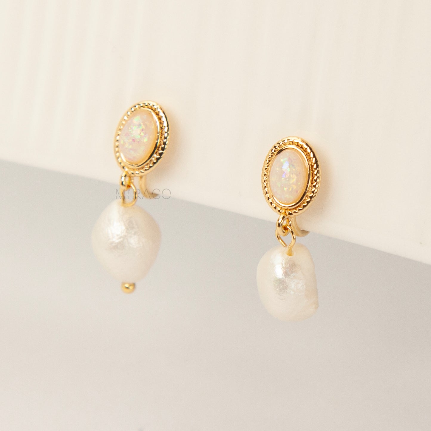 Pair of gold-tone, coil-back clip-on earrings with an oval, bezel-set iridescent opal-effect stone and a dangling real, irregularly shaped baroque freshwater pearl.