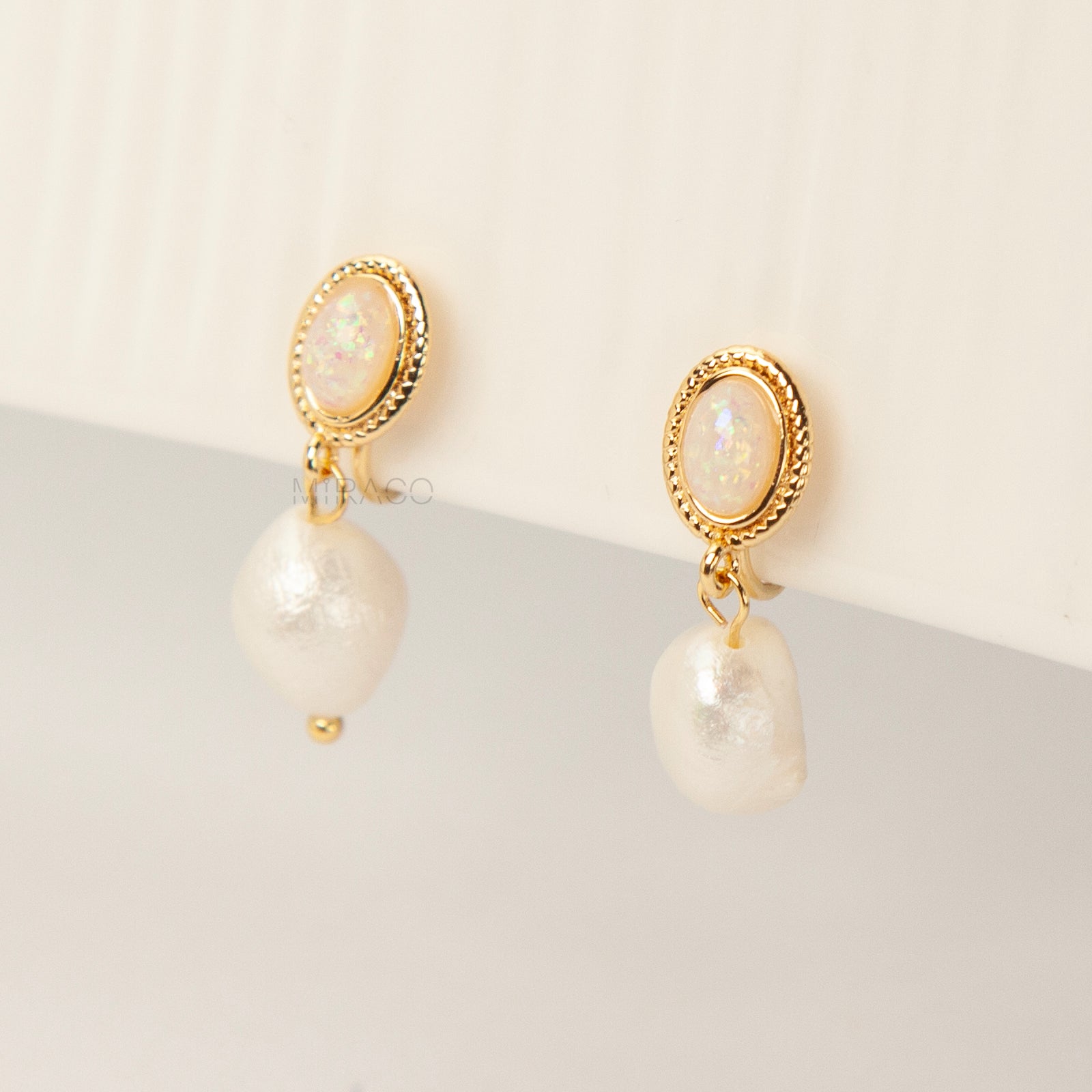 Pair of gold-tone, coil-back clip-on earrings with an oval, bezel-set iridescent opal-effect stone and a dangling real, irregularly shaped baroque freshwater pearl.