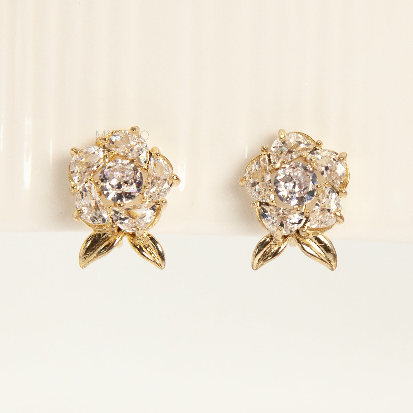 Pair of elegant gold-tone clip-on stud earrings shaped like a fully bloomed rose flower, set with a cluster of round and marquise-cut cubic zirconia stones, with a coil back clasp.