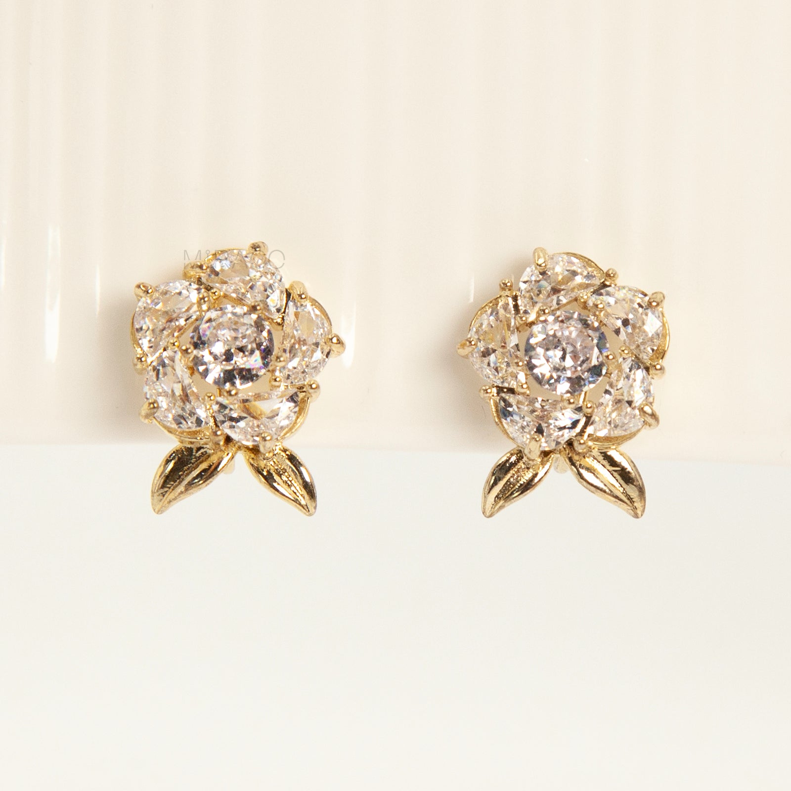 Pair of elegant gold-tone clip-on stud earrings shaped like a fully bloomed rose flower, set with a cluster of round and marquise-cut cubic zirconia stones, with a coil back clasp.