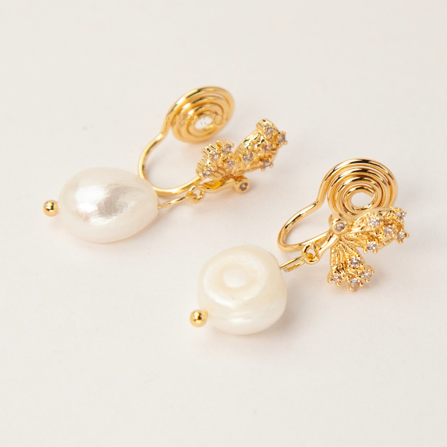 Pair of elegant gold-tone clip-on earrings with a CZ-encrusted butterfly swirl top and a dangling, lustrous white Baroque pearl drop, secured with a comfortable coil back clasp.