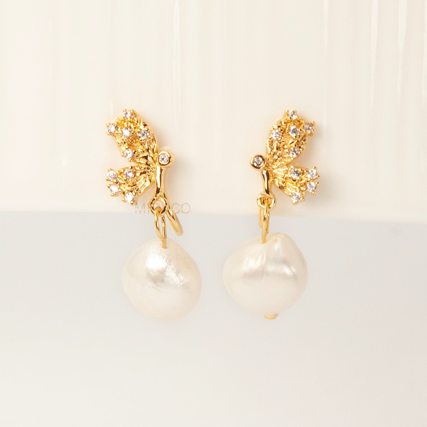 Pair of elegant gold-tone clip-on earrings with a CZ-encrusted butterfly swirl top and a dangling, lustrous white Baroque pearl drop, secured with a comfortable coil back clasp.