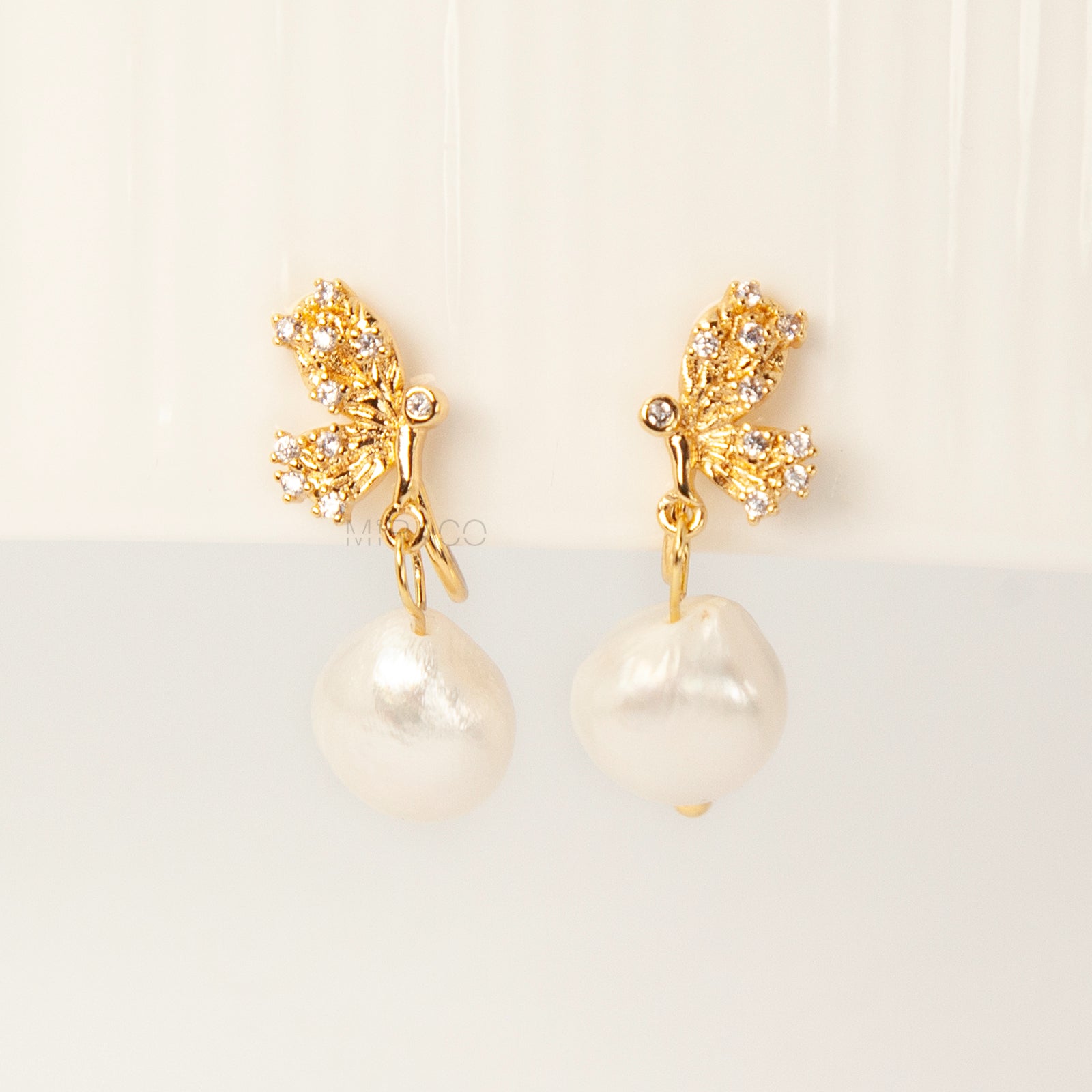 Pair of elegant gold-tone clip-on earrings with a CZ-encrusted butterfly swirl top and a dangling, lustrous white Baroque pearl drop, secured with a comfortable coil back clasp.