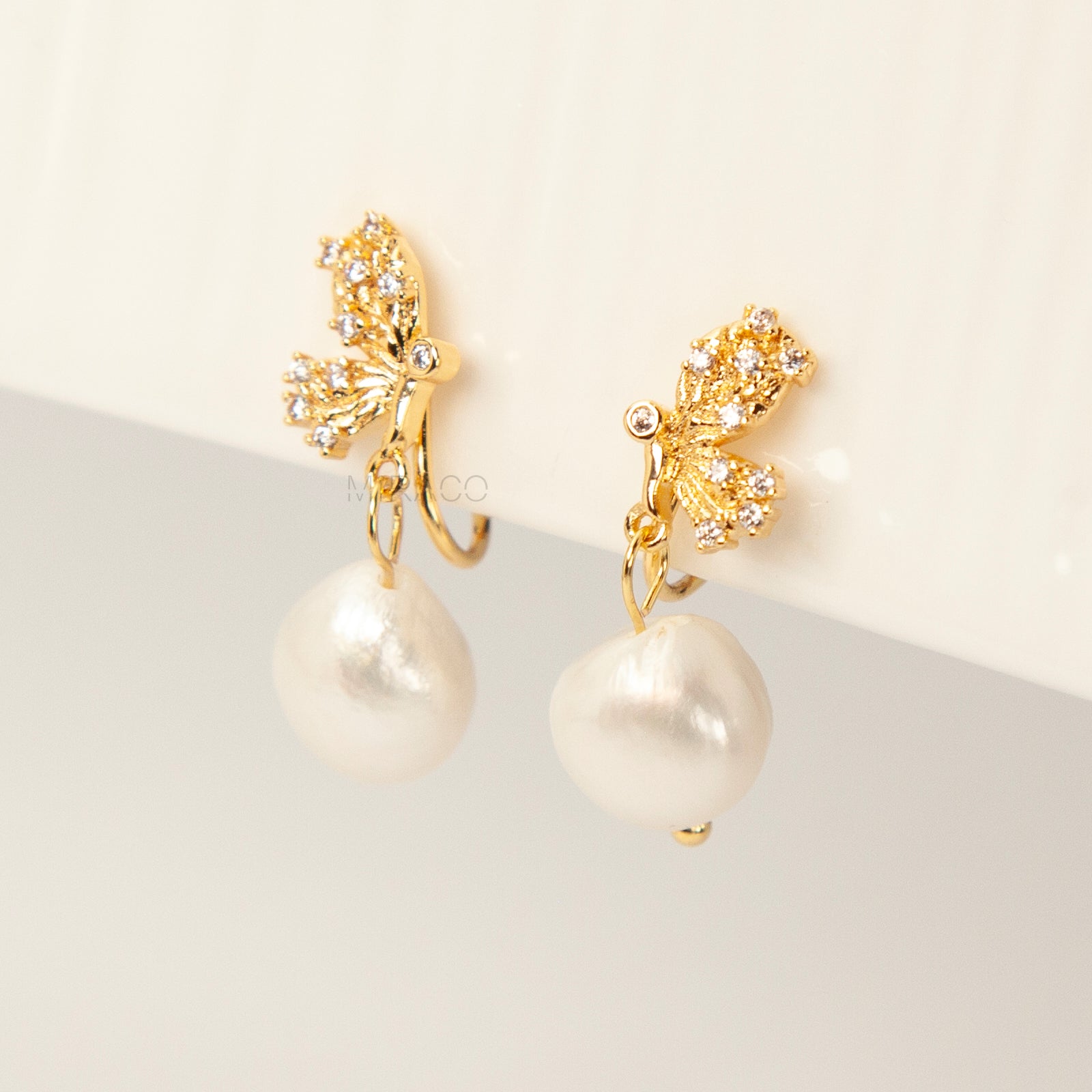 Pair of elegant gold-tone clip-on earrings with a CZ-encrusted butterfly swirl top and a dangling, lustrous white Baroque pearl drop, secured with a comfortable coil back clasp.