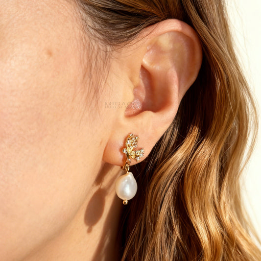 Pair of elegant gold-tone clip-on earrings with a CZ-encrusted butterfly swirl top and a dangling, lustrous white Baroque pearl drop, secured with a comfortable coil back clasp.