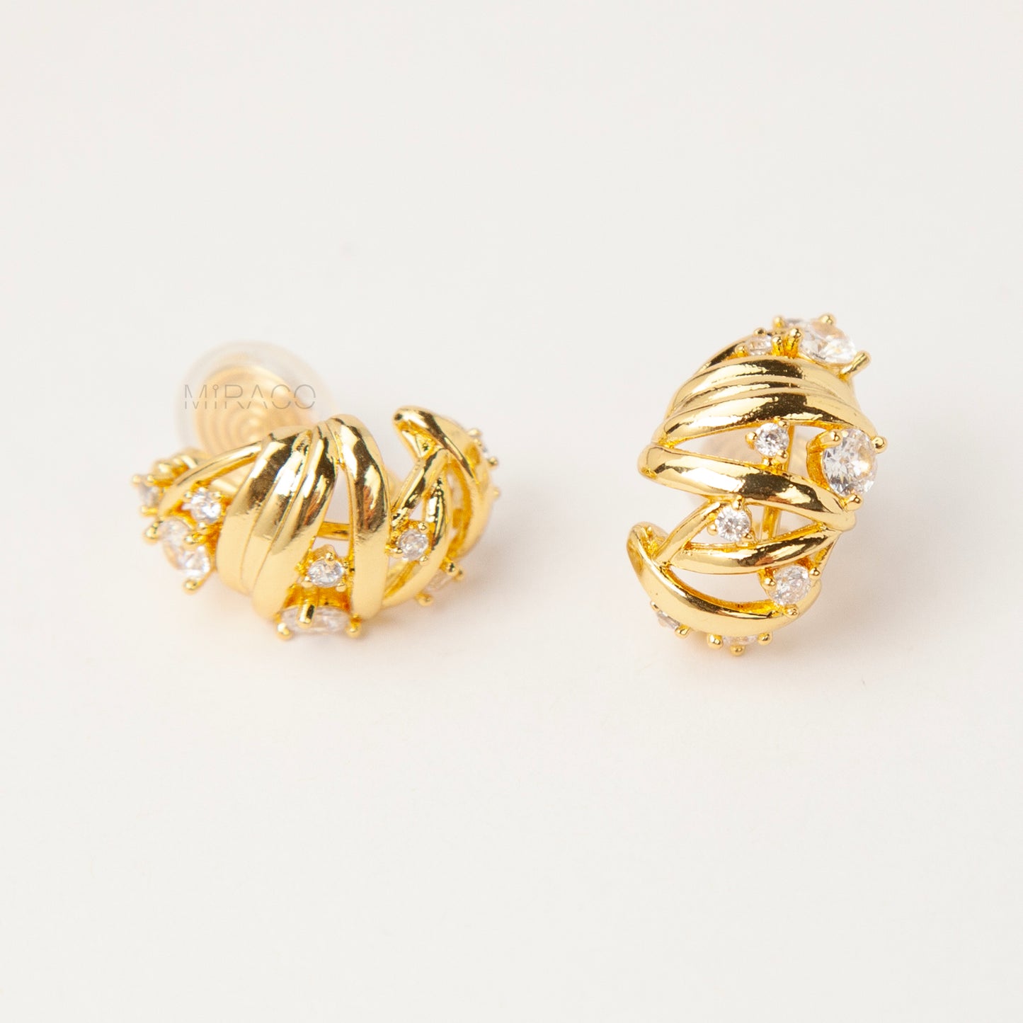 Gold clip-on earrings with wrapped sculptural design and clear crystal accents, featuring a comfortable coil back for non-pierced ears
