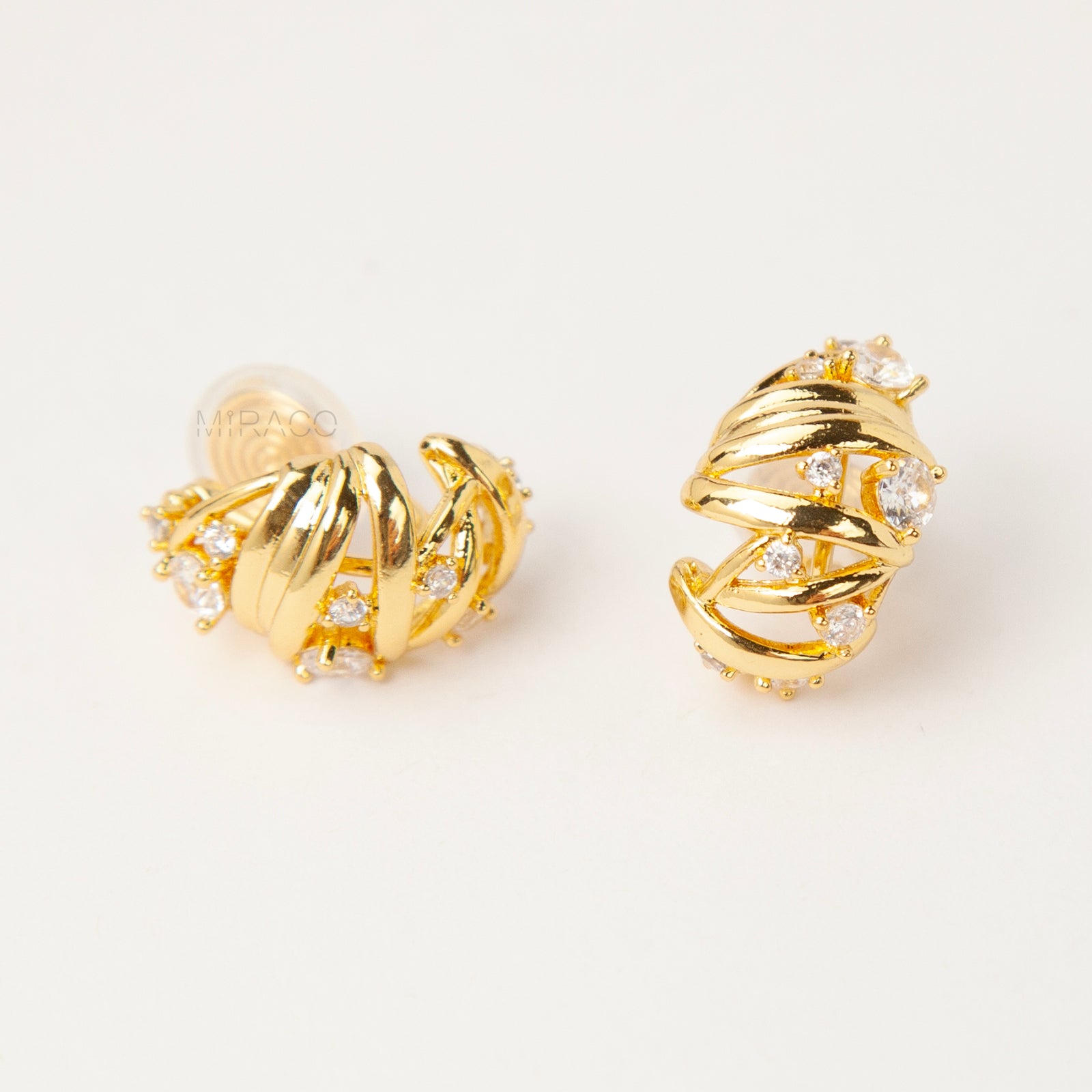 Gold clip-on earrings with wrapped sculptural design and clear crystal accents, featuring a comfortable coil back for non-pierced ears