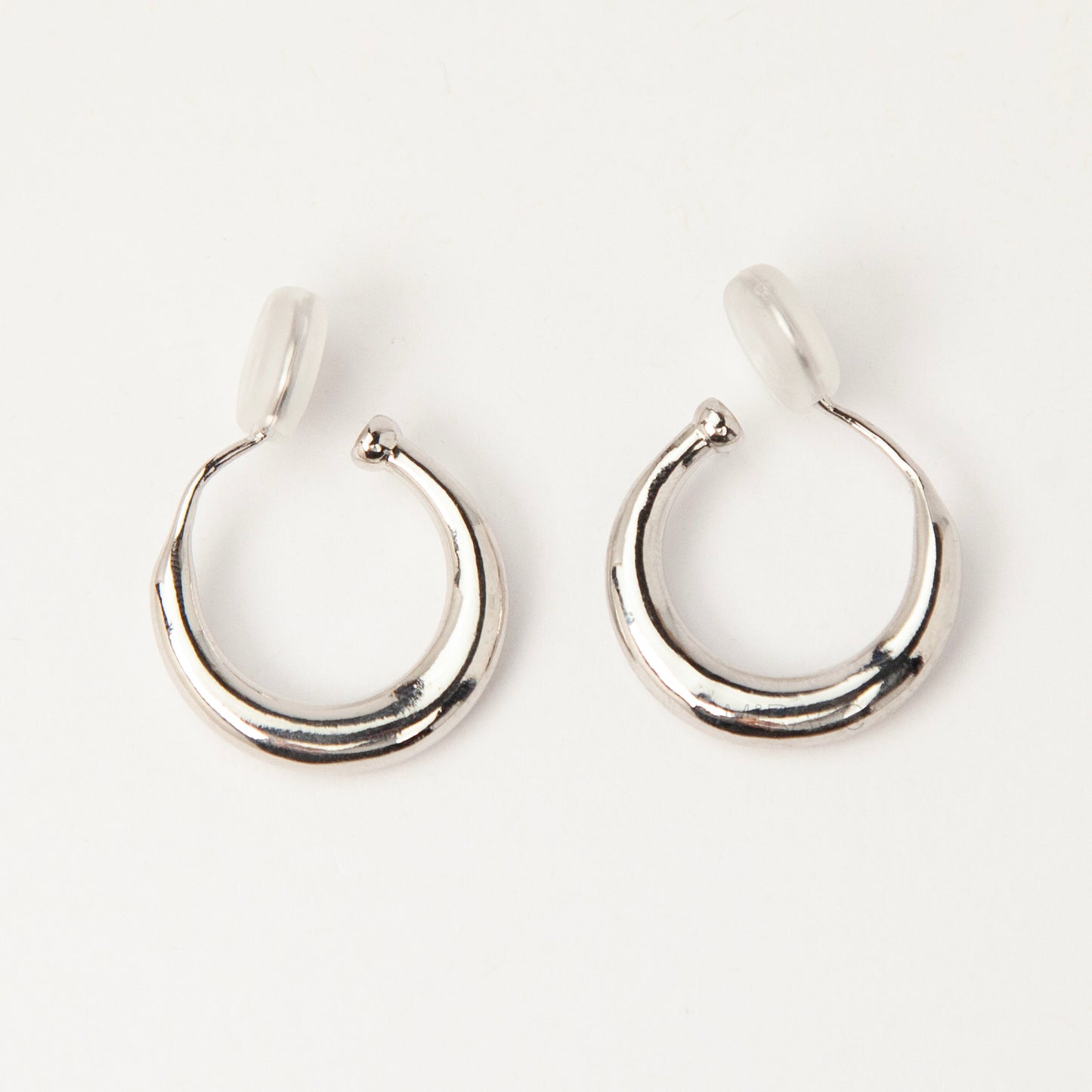 Pair of silver-tone tapered crescent hoop clip-on earrings with comfortable coil-back closures and clear silicone pads on a white background.