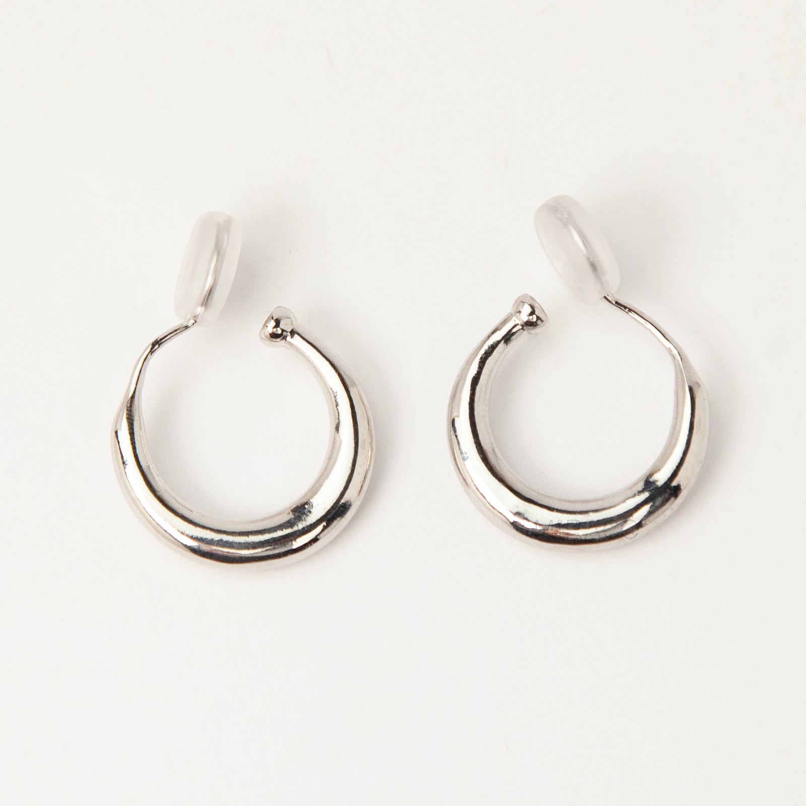 Pair of silver-tone tapered crescent hoop clip-on earrings with comfortable coil-back closures and clear silicone pads on a white background.