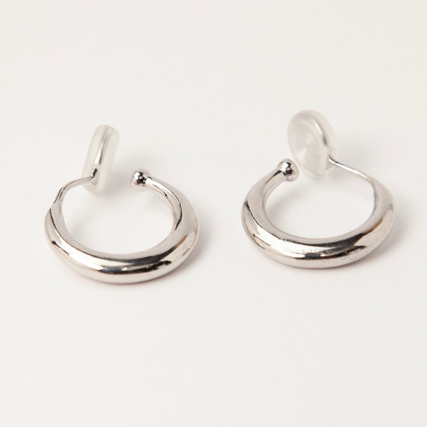 Pair of silver-tone tapered crescent hoop clip-on earrings with comfortable coil-back closures and clear silicone pads on a white background.