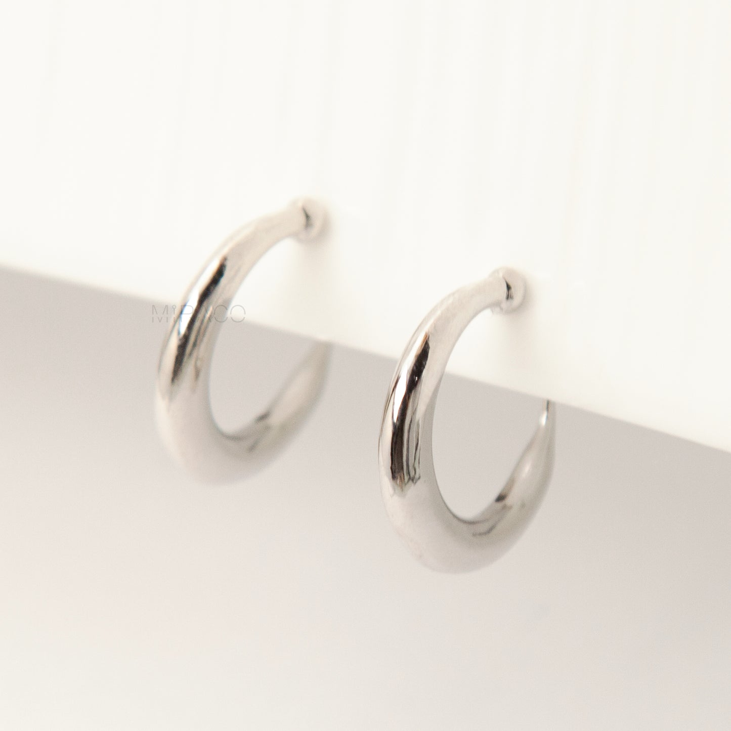 Pair of silver-tone tapered crescent hoop clip-on earrings with comfortable coil-back closures and clear silicone pads on a white background.