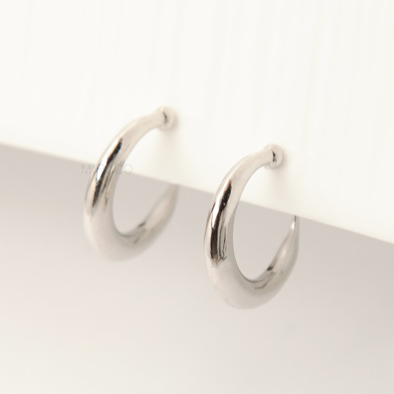 Pair of silver-tone tapered crescent hoop clip-on earrings with comfortable coil-back closures and clear silicone pads on a white background.