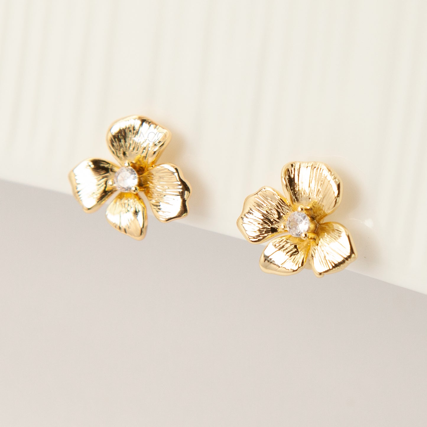 Pair of gold-tone textured flower-shaped clip-on earrings with a round clear crystal center and comfortable coil-back closures on a white background.