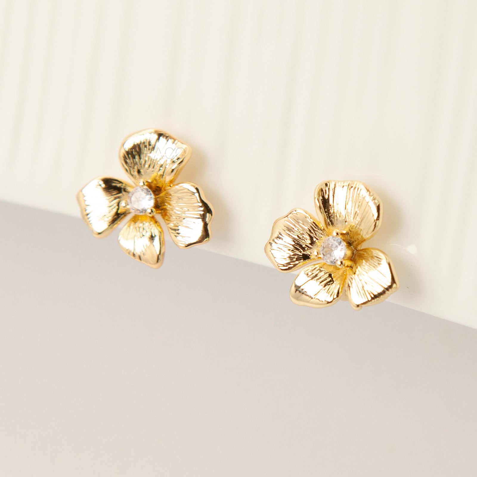 Pair of gold-tone textured flower-shaped clip-on earrings with a round clear crystal center and comfortable coil-back closures on a white background.