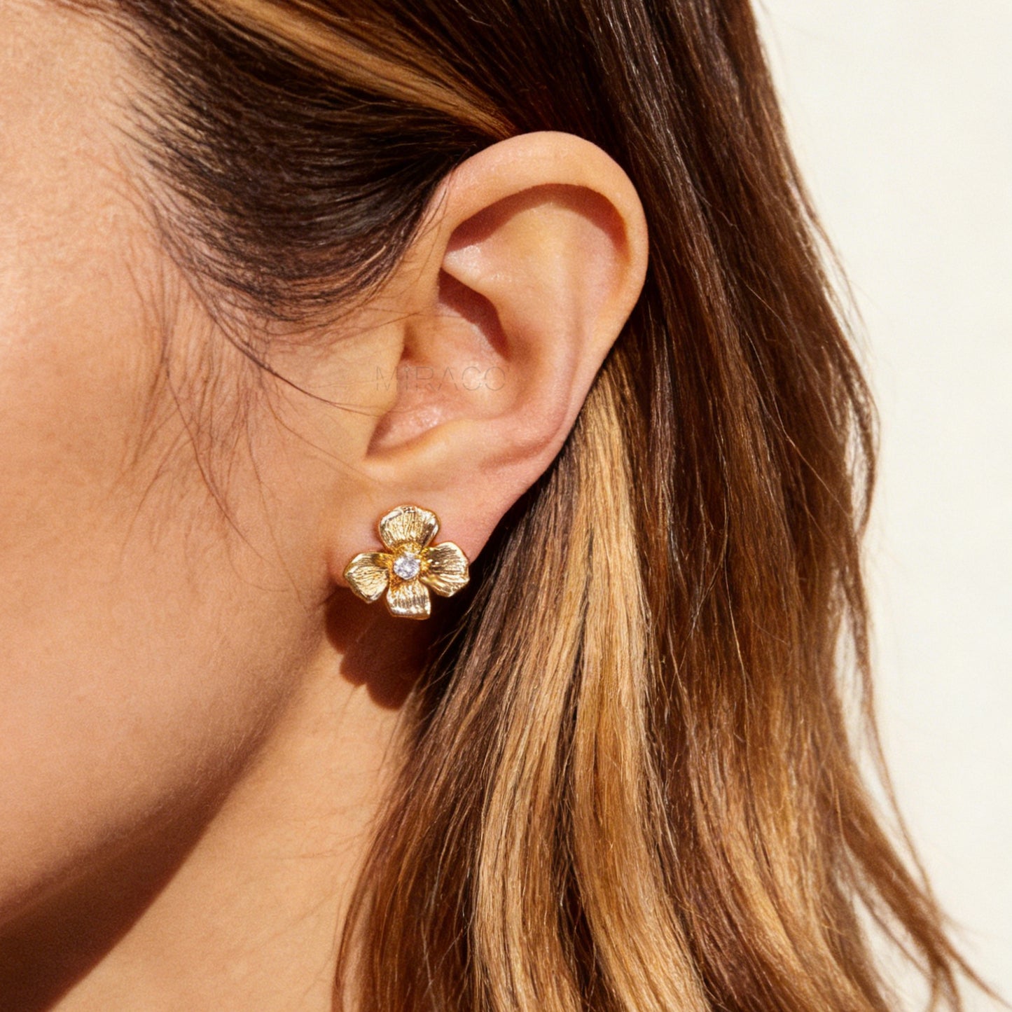 Pair of gold-tone textured flower-shaped clip-on earrings with a round clear crystal center and comfortable coil-back closures on a white background.