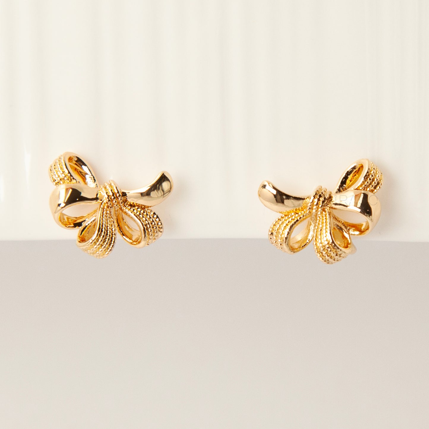 Pair of gold-tone multi-loop bow ribbon clip-on earrings featuring textured detailing and comfortable coil-back closures with clear silicone pads.
