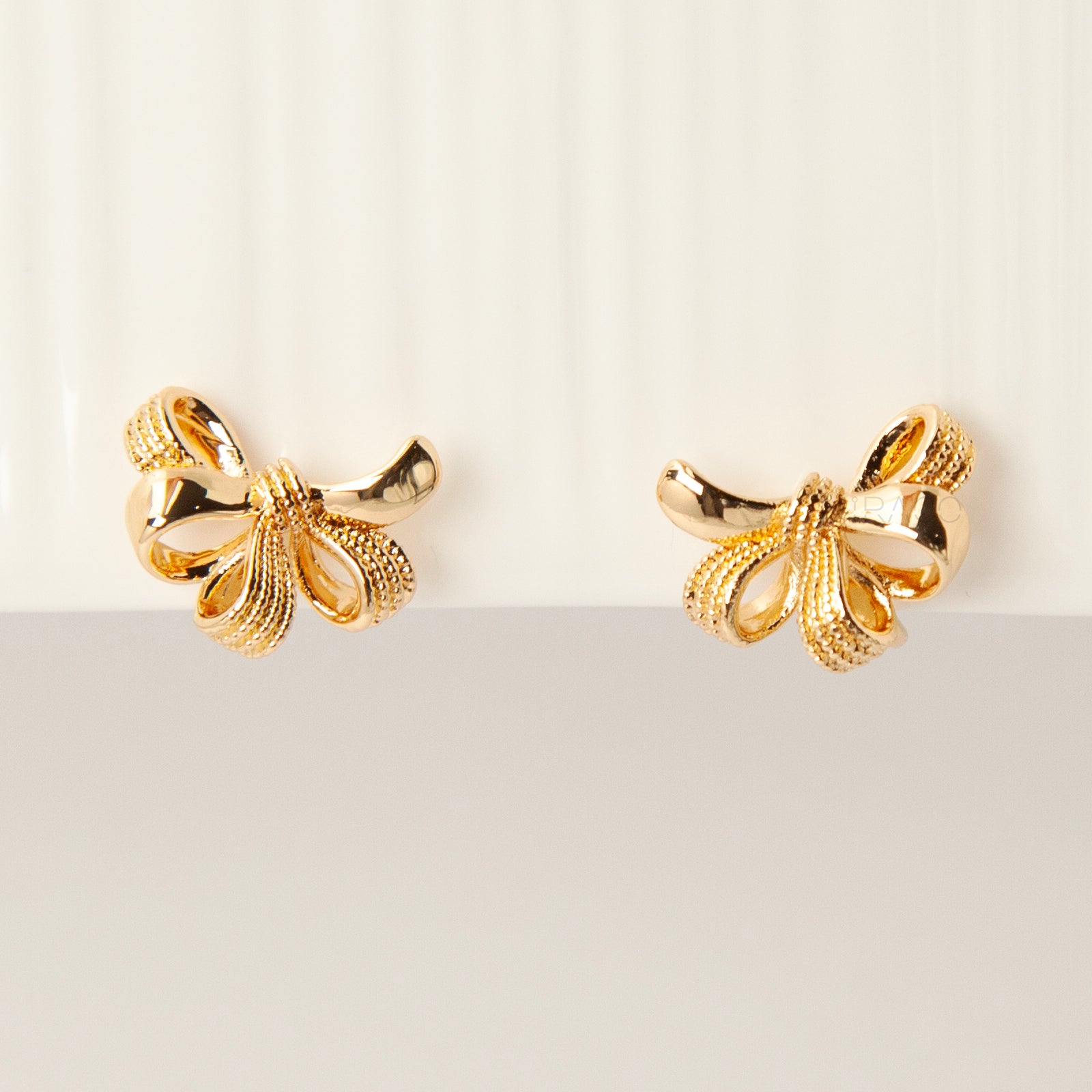 Pair of gold-tone multi-loop bow ribbon clip-on earrings featuring textured detailing and comfortable coil-back closures with clear silicone pads.