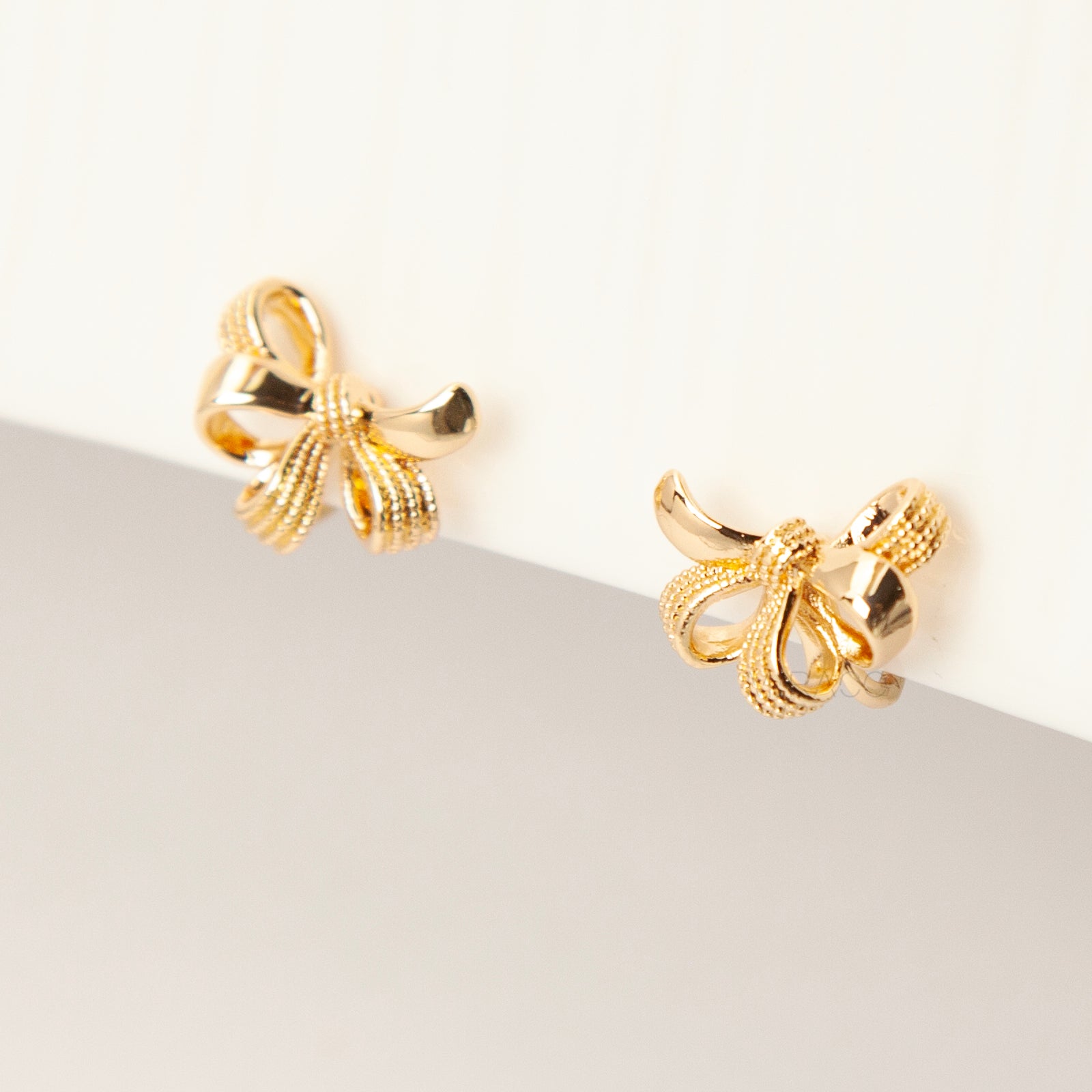 Pair of gold-tone multi-loop bow ribbon clip-on earrings featuring textured detailing and comfortable coil-back closures with clear silicone pads.