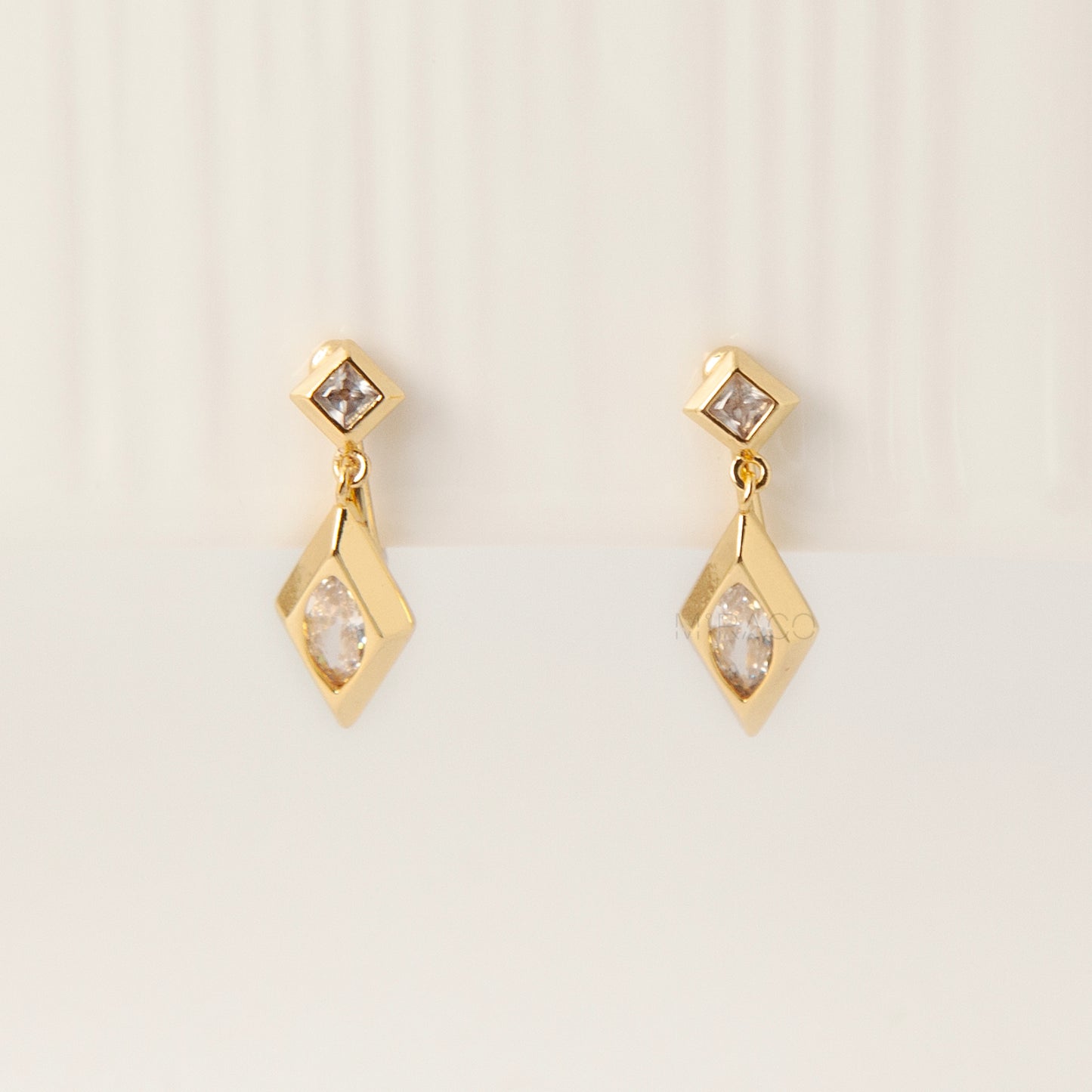 Pair of gold-tone geometric drop clip-on earrings featuring a small square crystal and a larger marquise-cut crystal dangle with comfortable coil-back closures.
