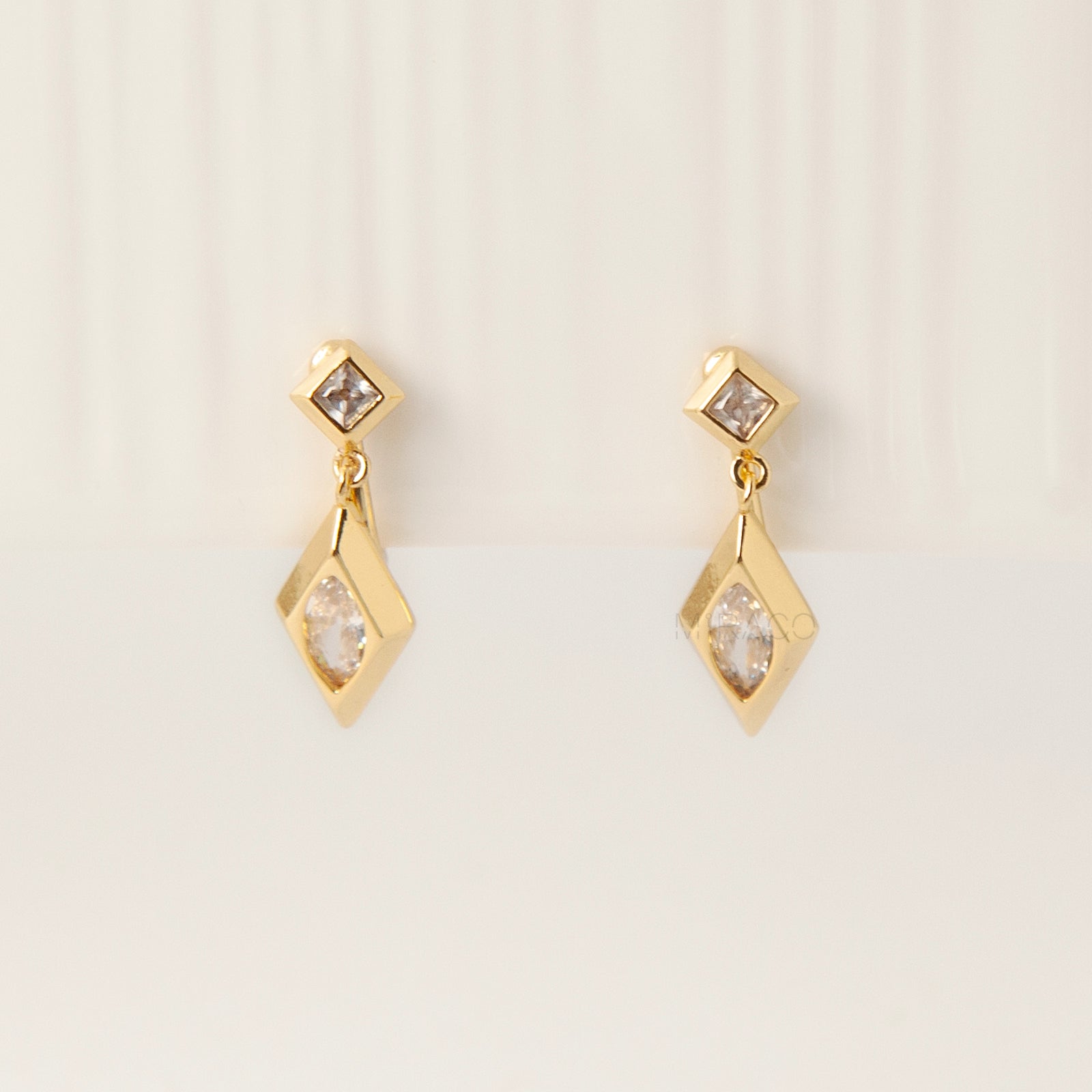 Pair of gold-tone geometric drop clip-on earrings featuring a small square crystal and a larger marquise-cut crystal dangle with comfortable coil-back closures.