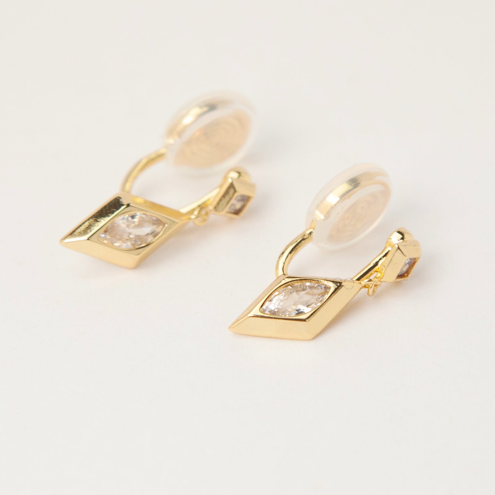Pair of gold-tone geometric drop clip-on earrings featuring a small square crystal and a larger marquise-cut crystal dangle with comfortable coil-back closures.