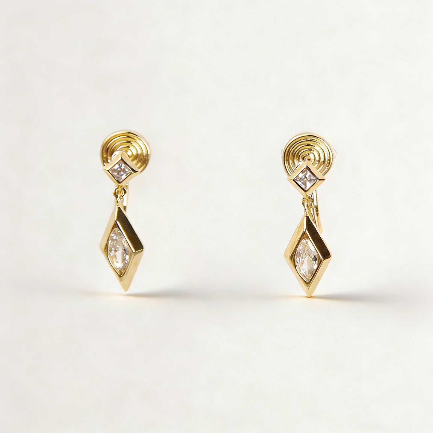 Pair of gold-tone geometric drop clip-on earrings featuring a small square crystal and a larger marquise-cut crystal dangle with comfortable coil-back closures.