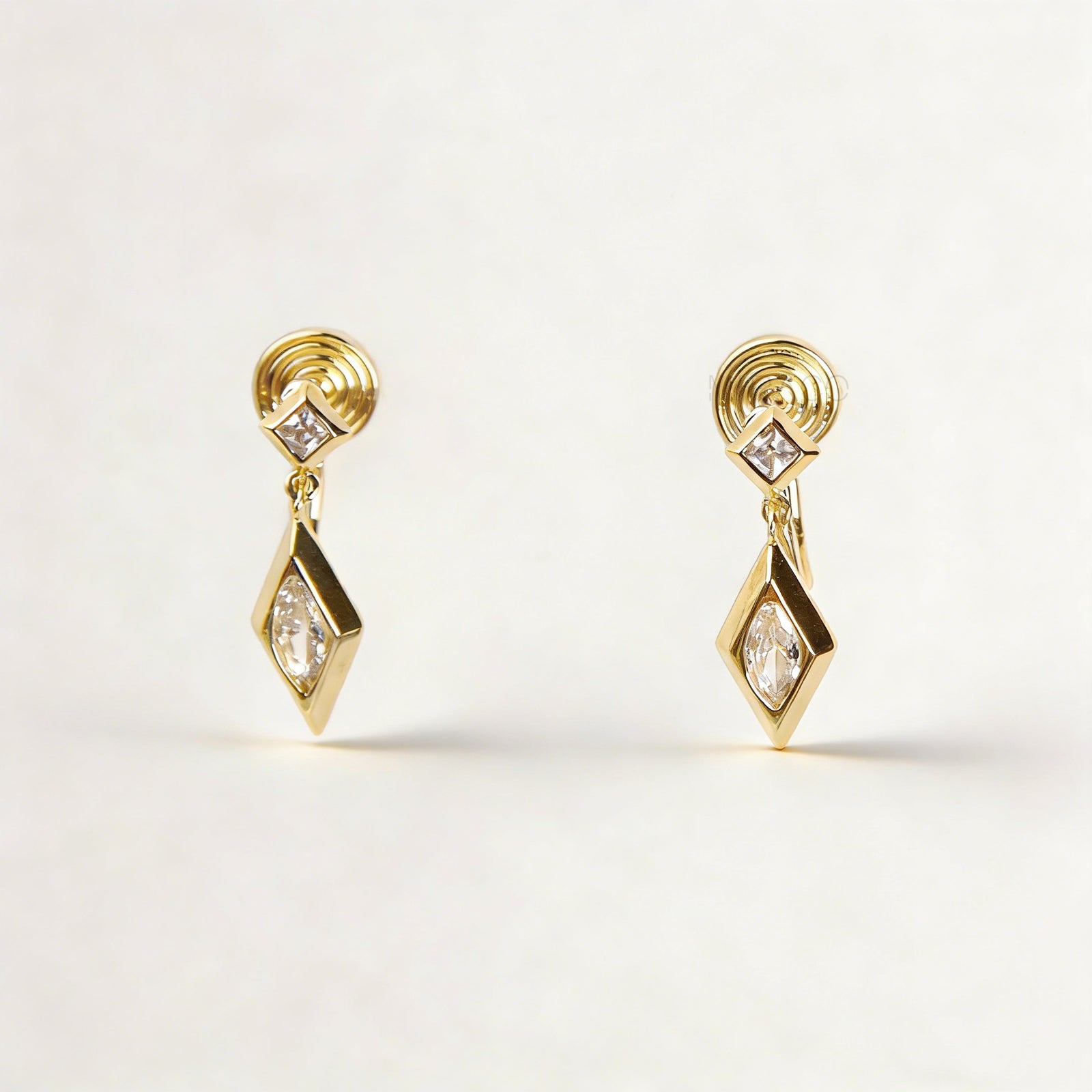 Pair of gold-tone geometric drop clip-on earrings featuring a small square crystal and a larger marquise-cut crystal dangle with comfortable coil-back closures.