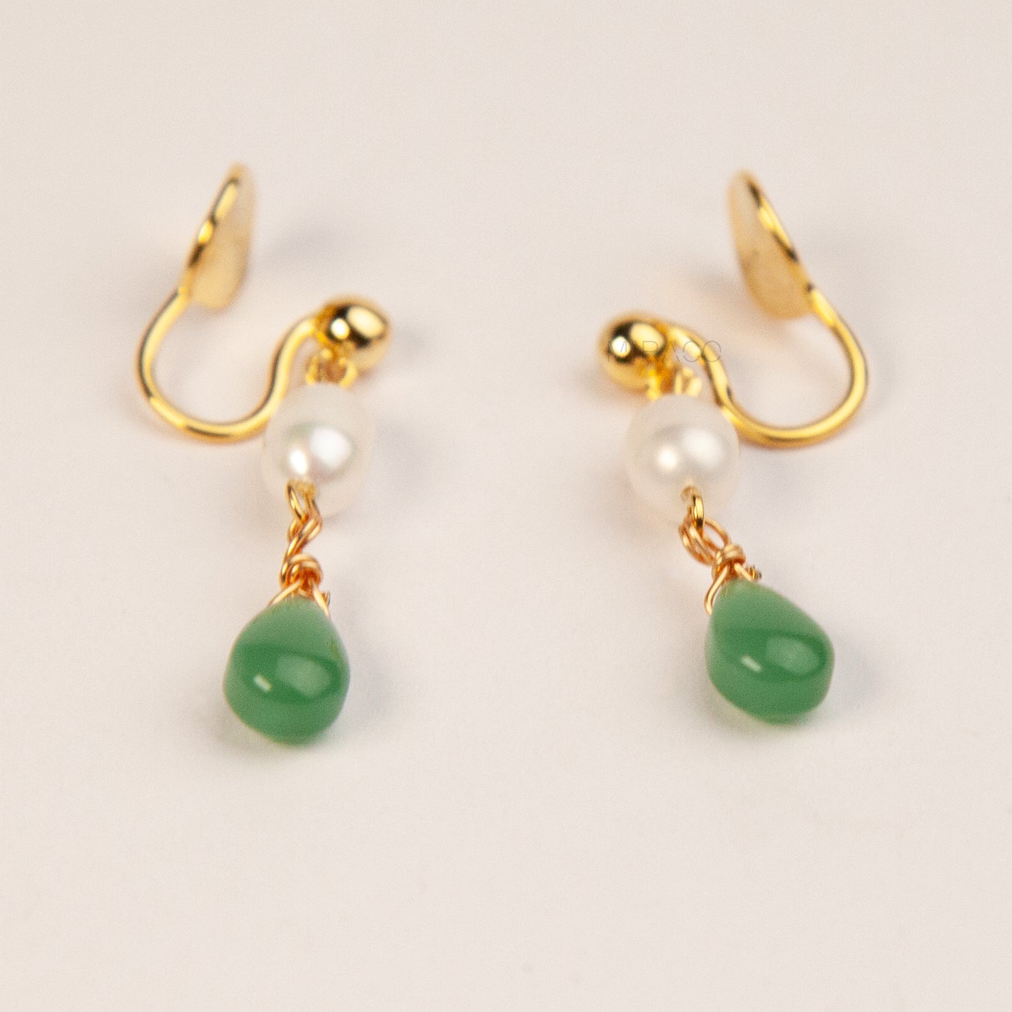 A pair of gold clip-on earrings featuring a comfortable coil back mechanism, a white oval pearl, and a dangling green jade teardrop stone.