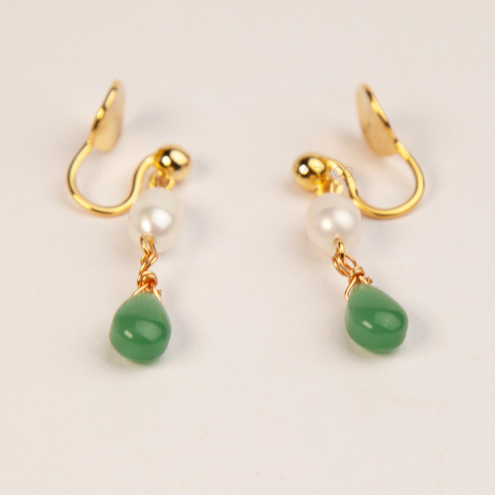 A pair of gold clip-on earrings featuring a comfortable coil back mechanism, a white oval pearl, and a dangling green jade teardrop stone.
