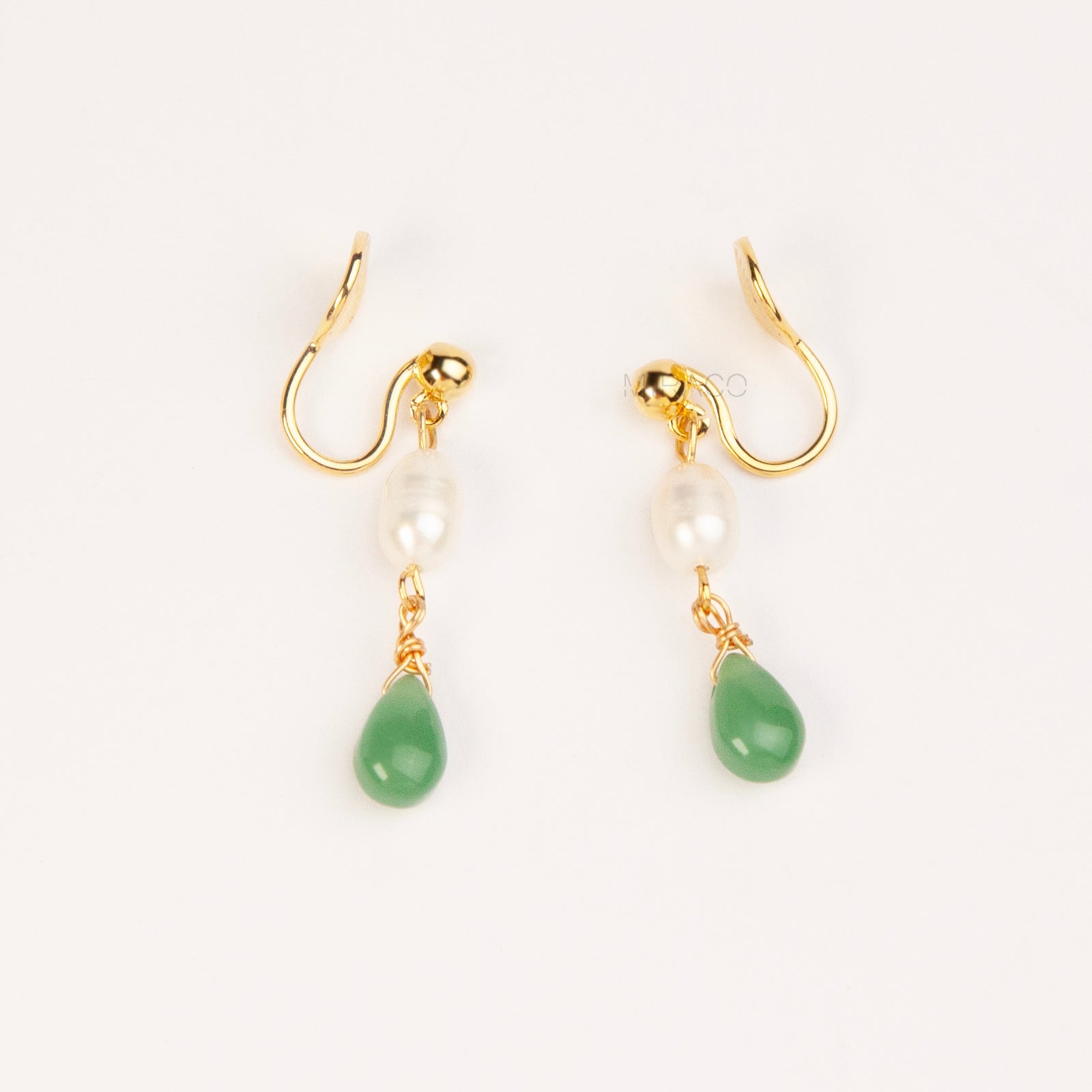 A pair of gold clip-on earrings featuring a comfortable coil back mechanism, a white oval pearl, and a dangling green jade teardrop stone.